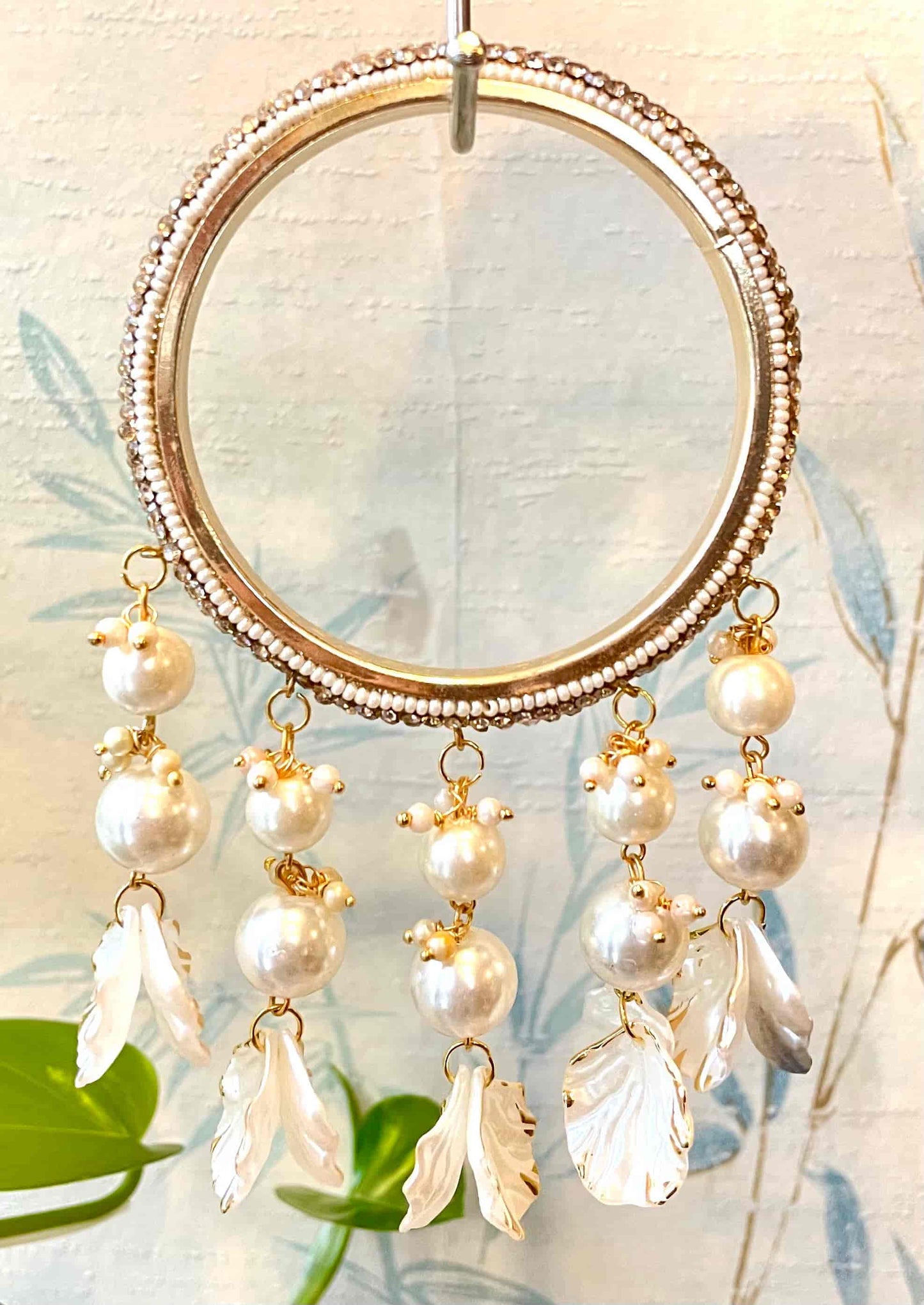 Sparkly golden bangle with hanging pearl and shell designs on a blurred natural background