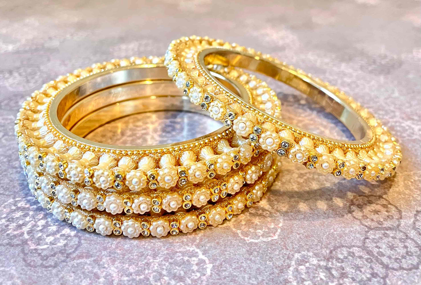 Set of 4 golden bangles with pearls organised as flowers on a reflective surace.