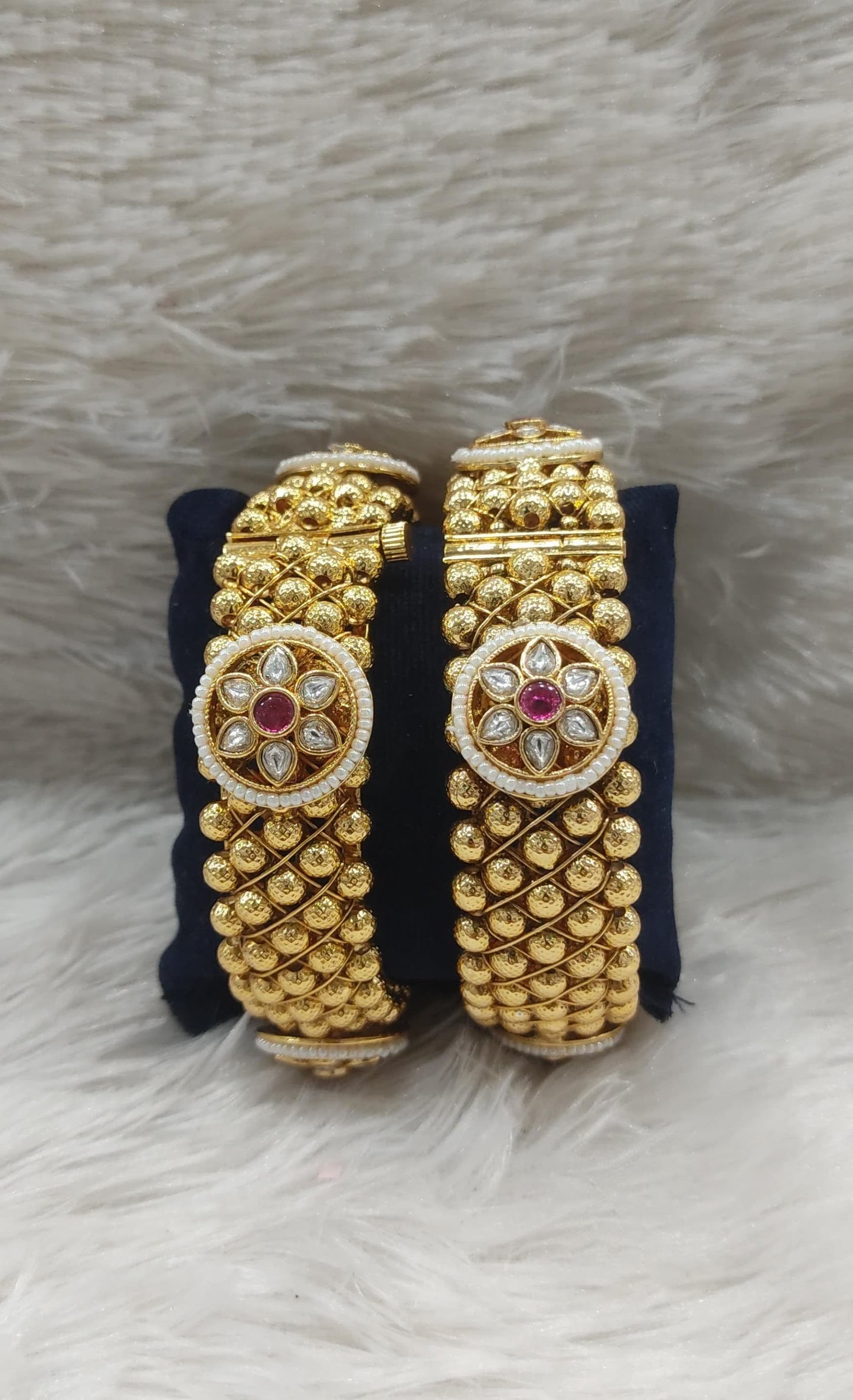 Pair of gold bangles with intricate floral designs on a soft fabric background