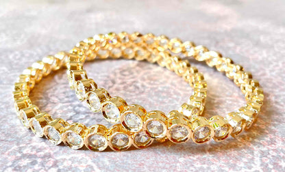 Two gold bracelets/bangles with clear stones on a light background