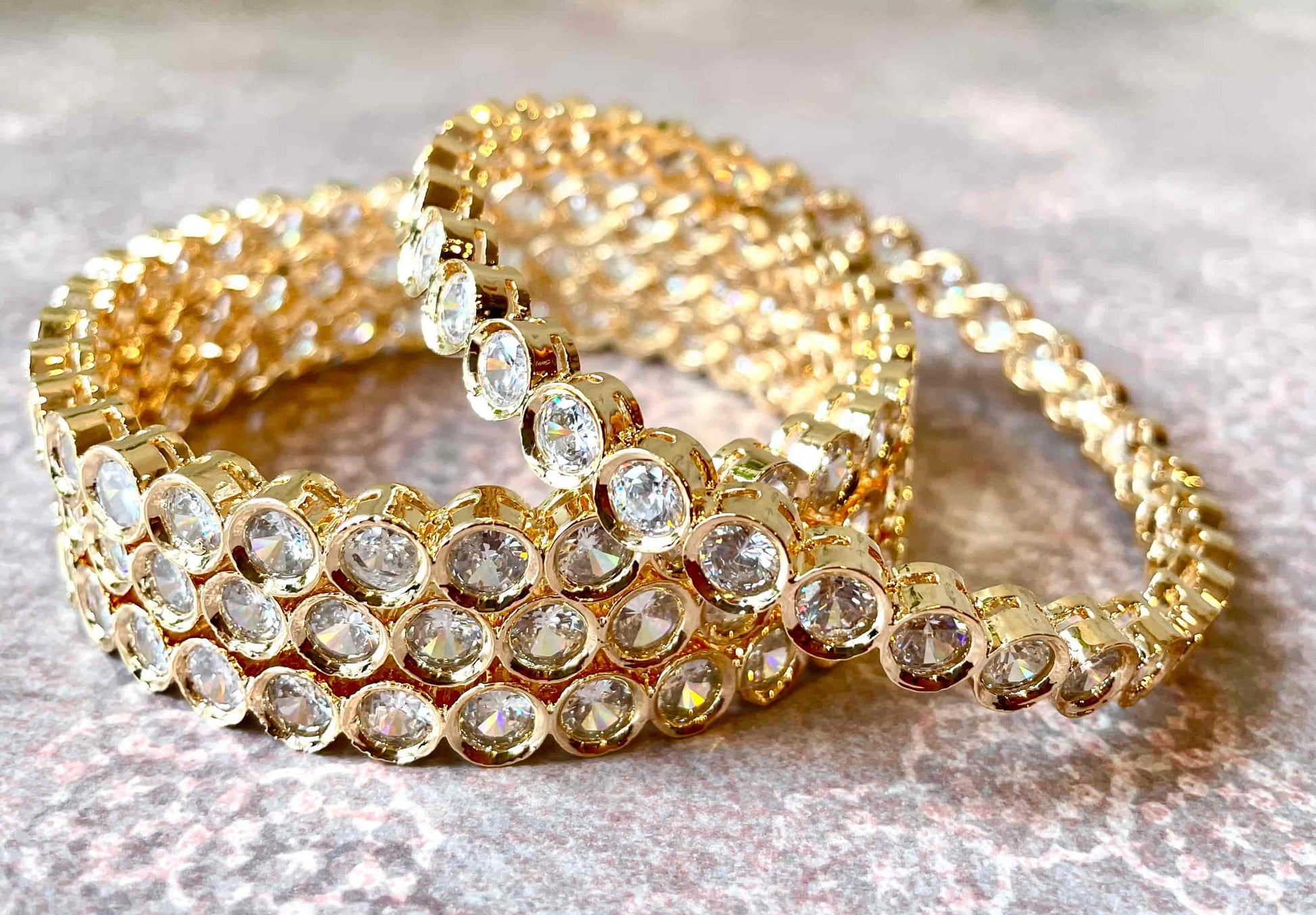 Set of 4 gold bracelets/bangles with clear gemstones on a textured surface