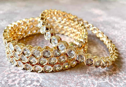 Set of 4 gold bracelets/bangles with clear gemstones on a textured surface