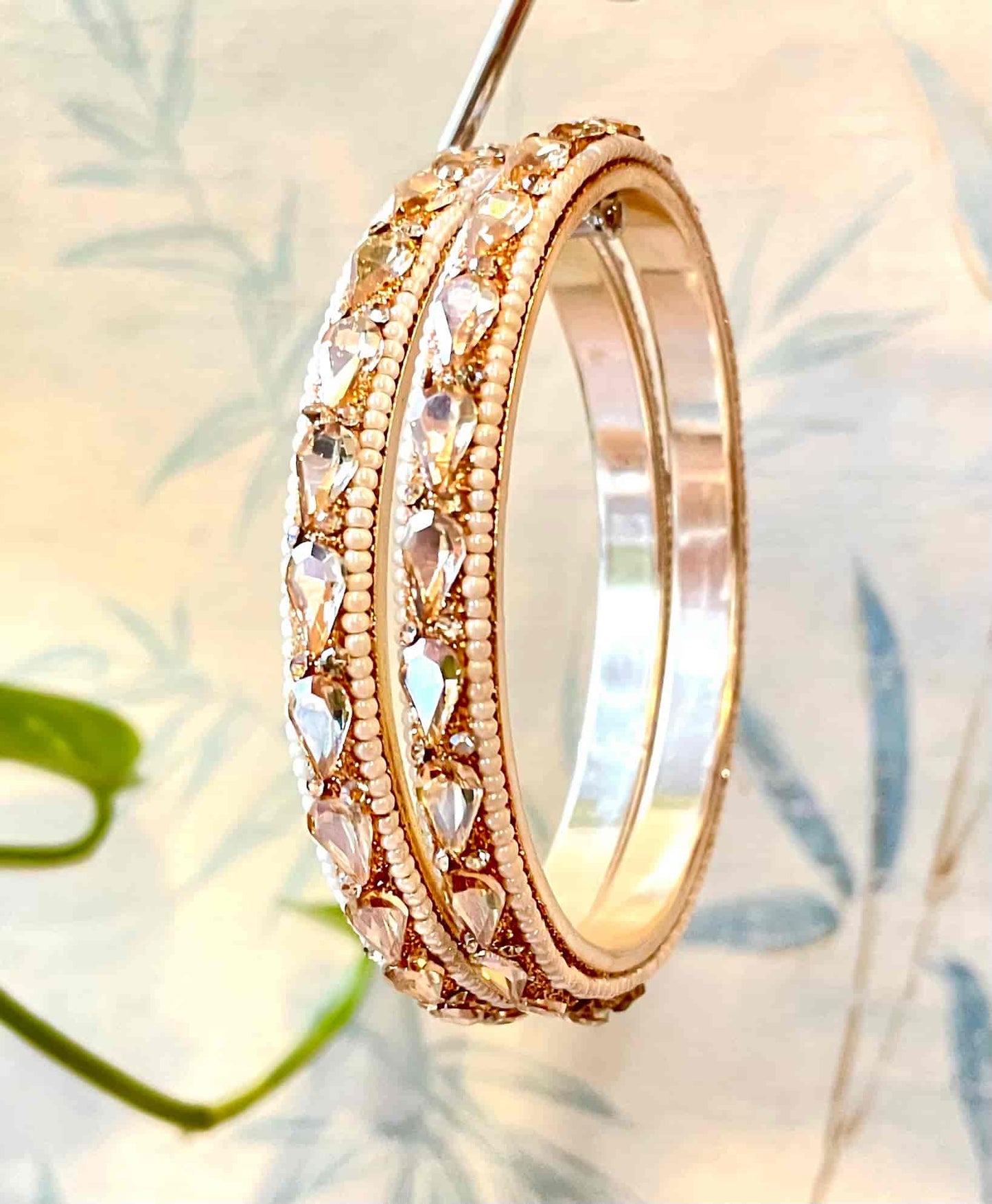 Golden bangles with clear gemstones shaped as water droplets on a soft focus background