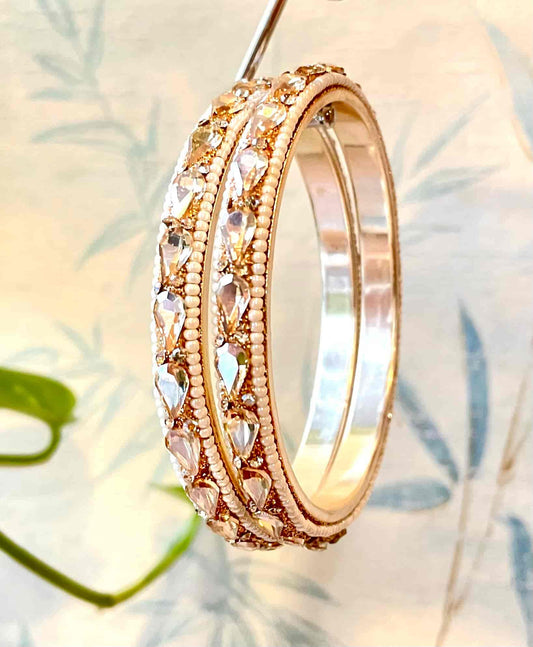 Golden bangles with clear gemstones shaped as water droplets on a soft focus background