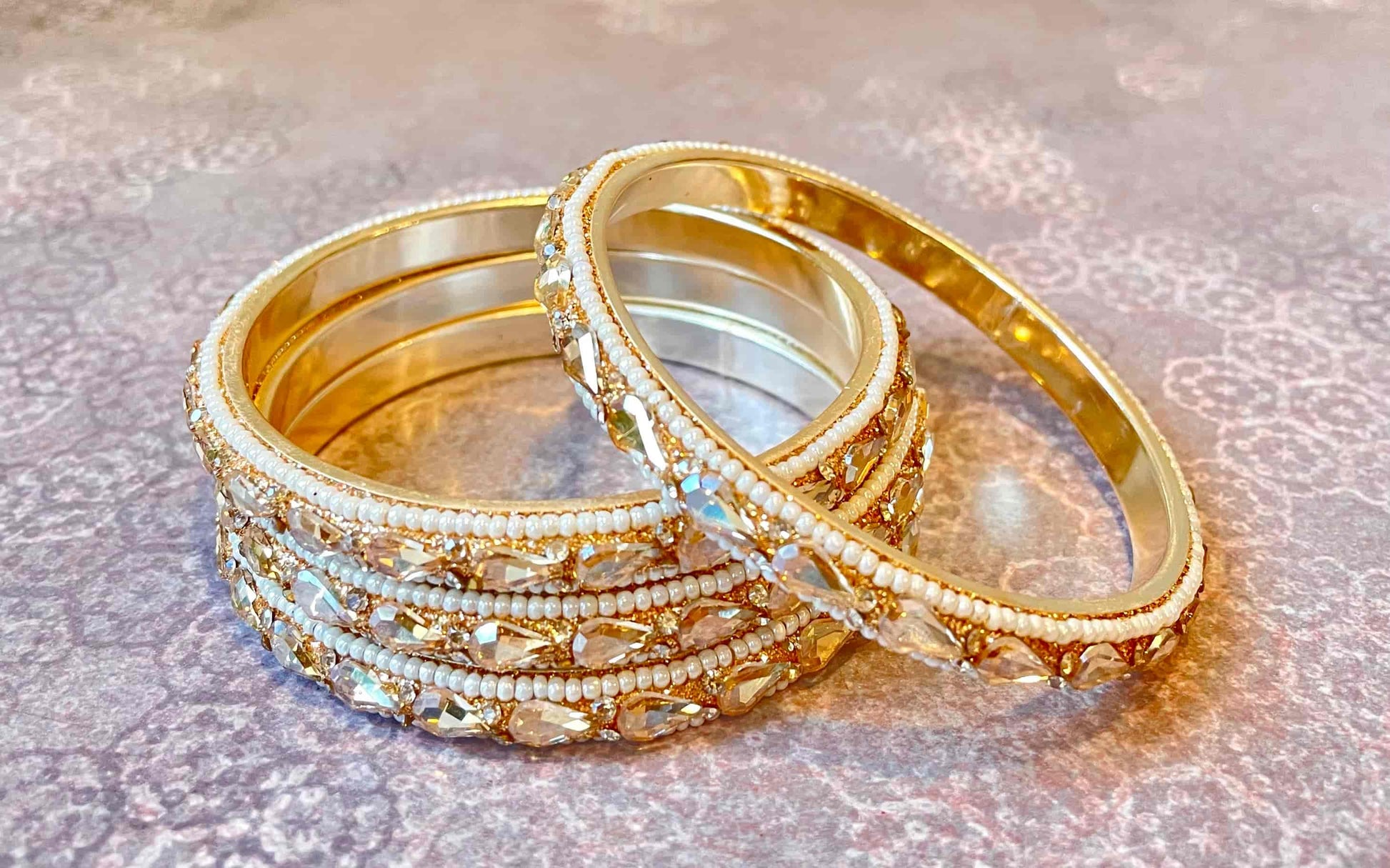 Set of golden bangles with clear gemstones shaped as water droplets on a textured surface