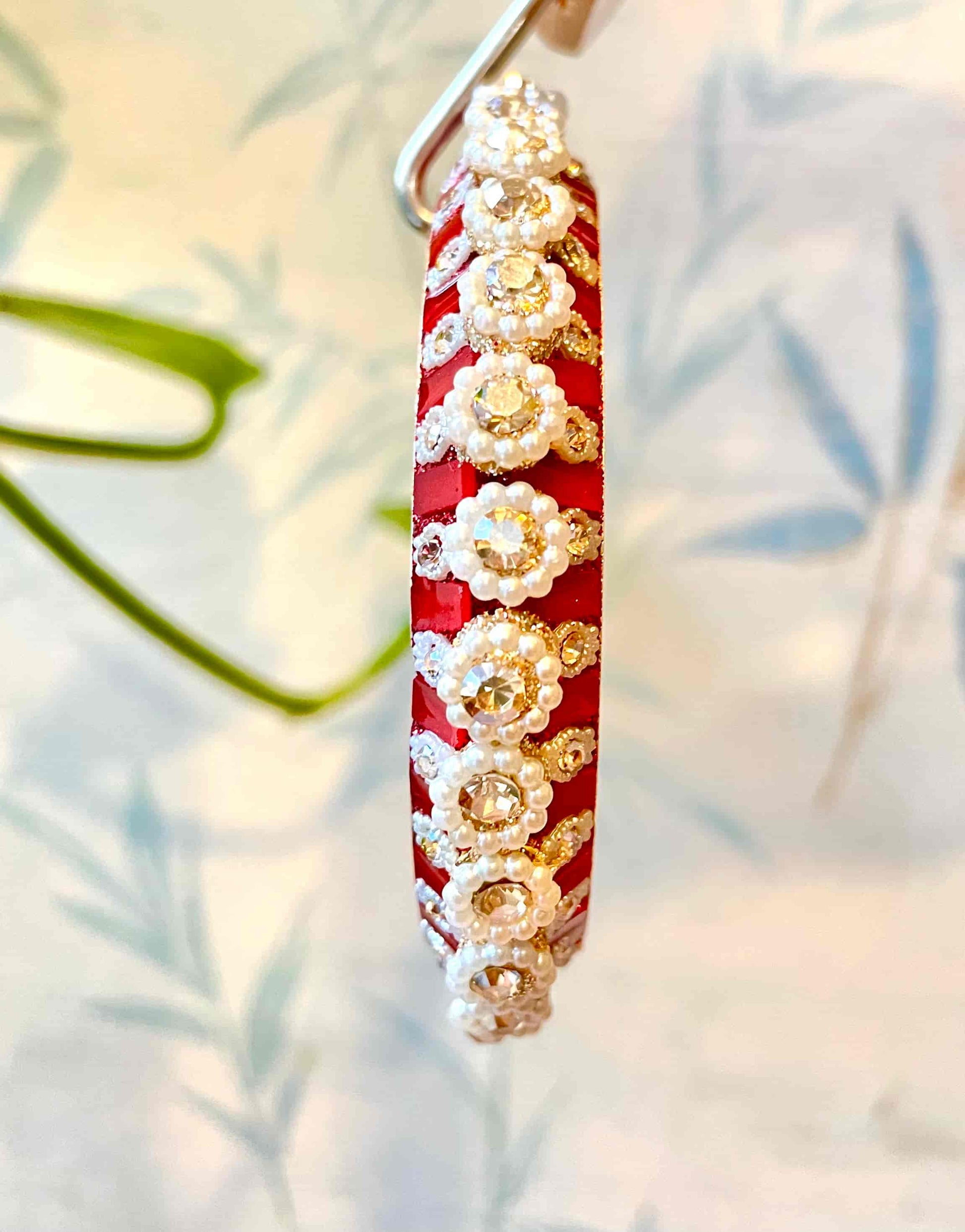 Red and gold bangles with diamond accents and pearls surrounding them on a soft natural background