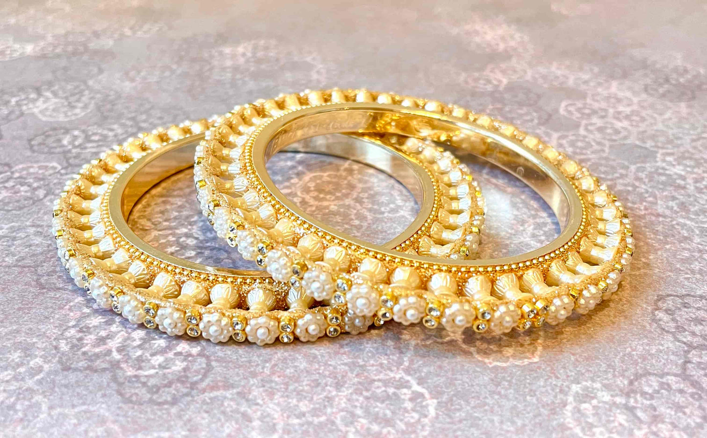 Two golden bangles with pearls organised in the shape of a flower on a textured surface