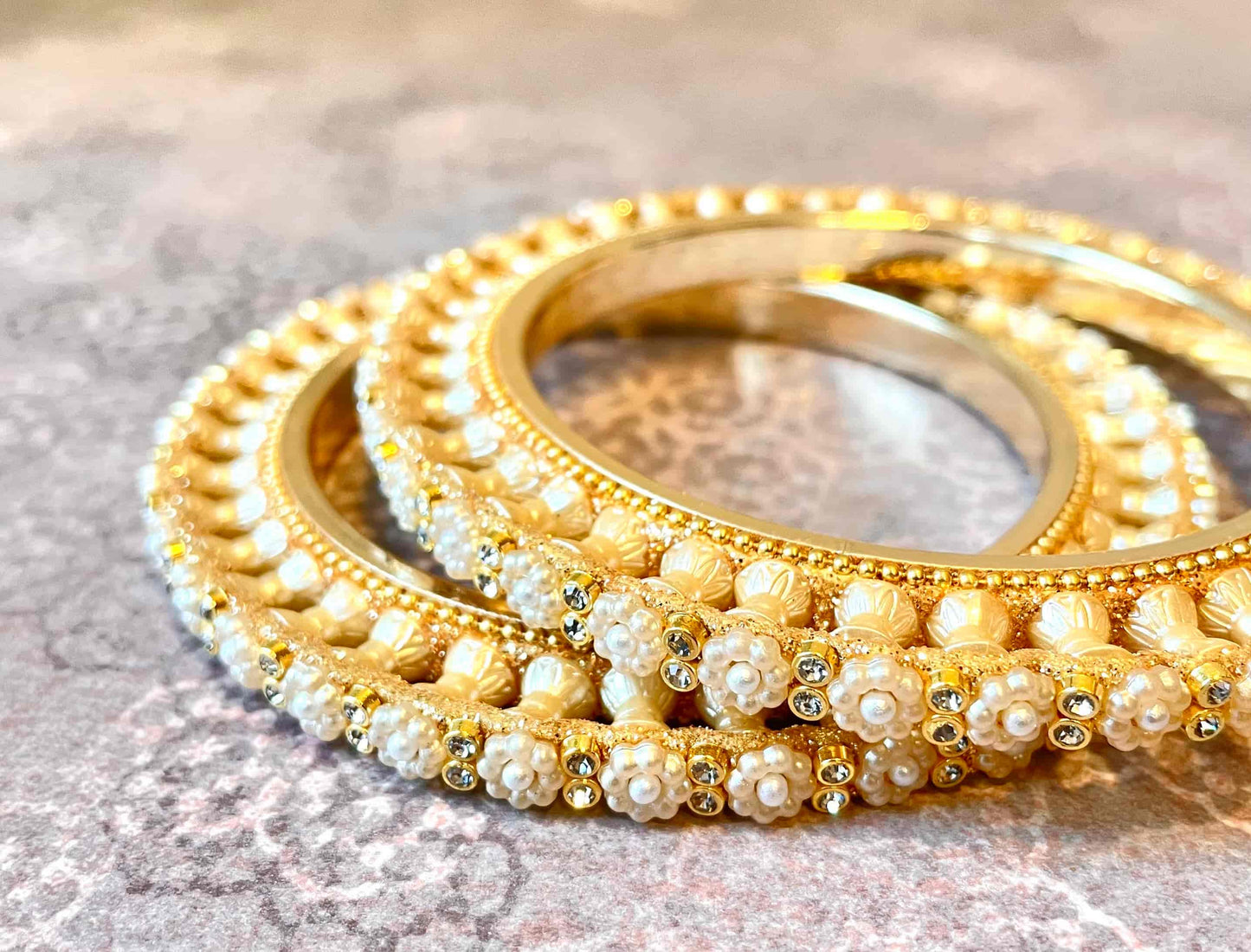 Golden bangles with pearls organised in the shape of a flower on a reflective surface