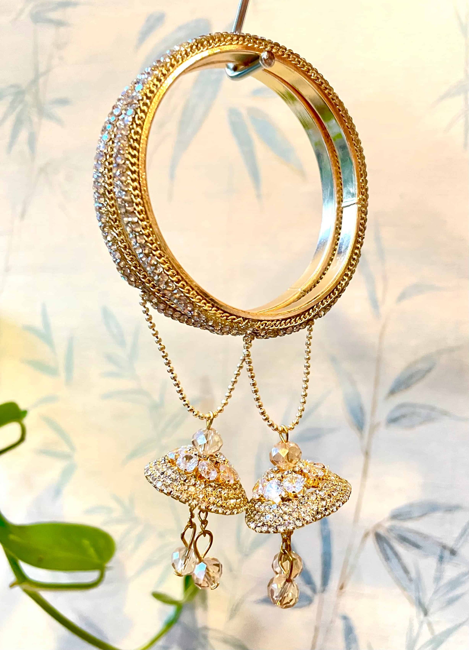 A pair of golden bangles with intricate designs and a hanging pendant on a soft, natural background