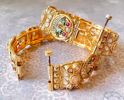 Gold bangles with gemstones and intricate peacock motifs on a textured gray background