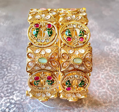 Gold bangles with gemstones and intricate peacock motifs on a textured gray background