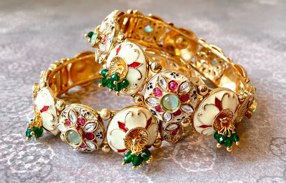 Gold bracelets/bangles with white and colourful decorative elements and gemstones on a light background