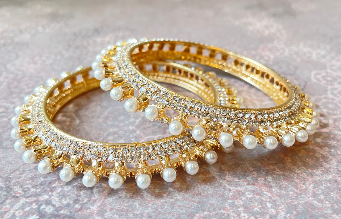 Pair of gold bangles with pearl embellishments on a light background