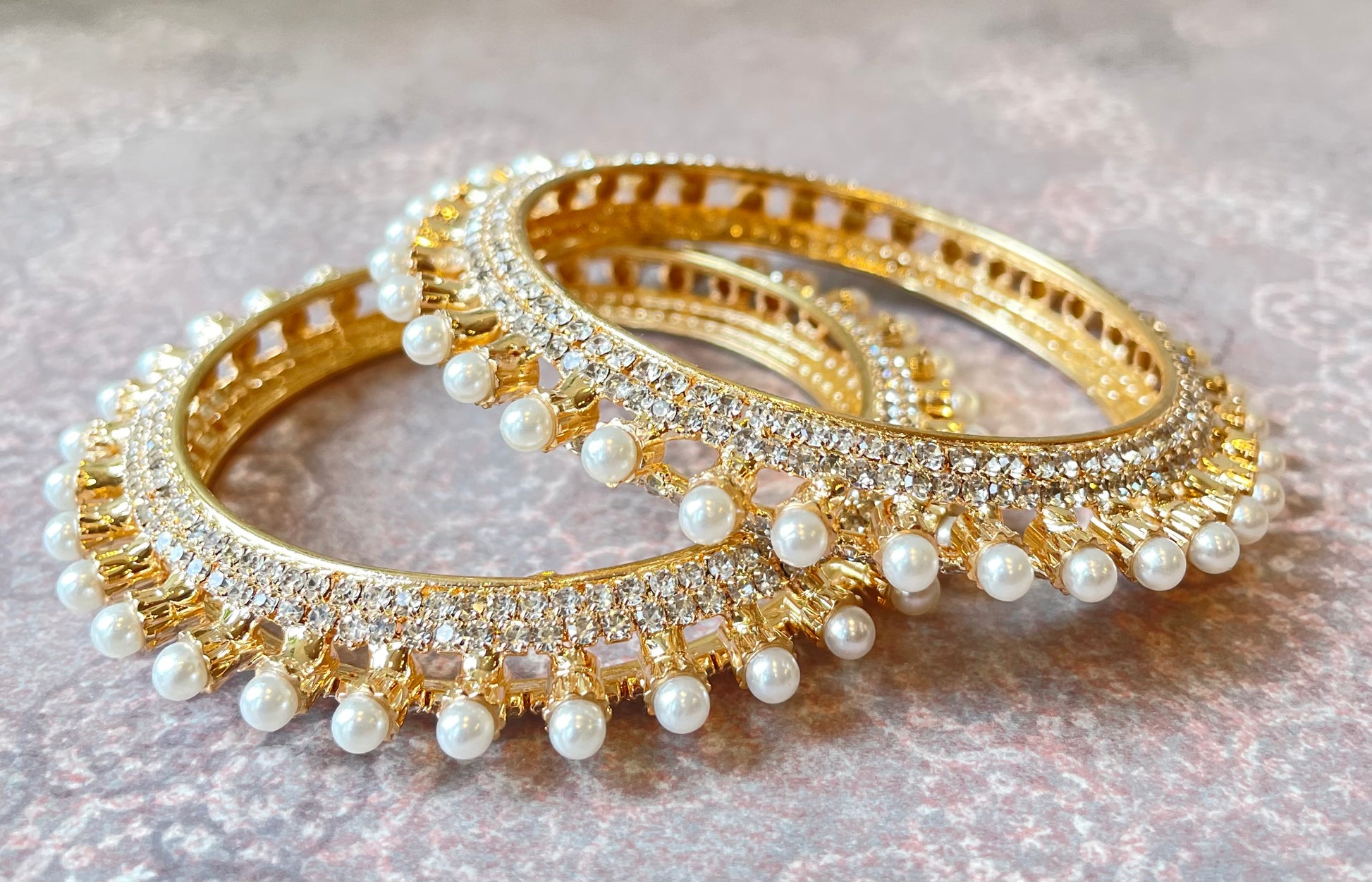 Pair of gold bangles with pearl embellishments on a light background