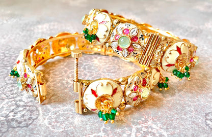 Gold bracelets/bangles with white and colourful decorative elements and gemstones on a light background